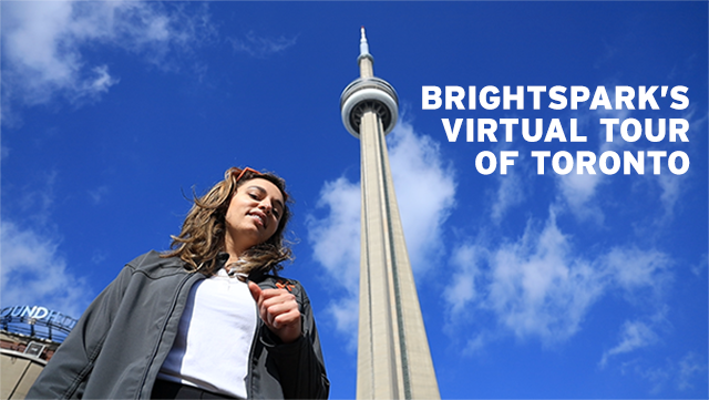 Brightspark Tour Leader Tamara stands in front of the CN Tower with bright blue sky on a walking tour of Toronto